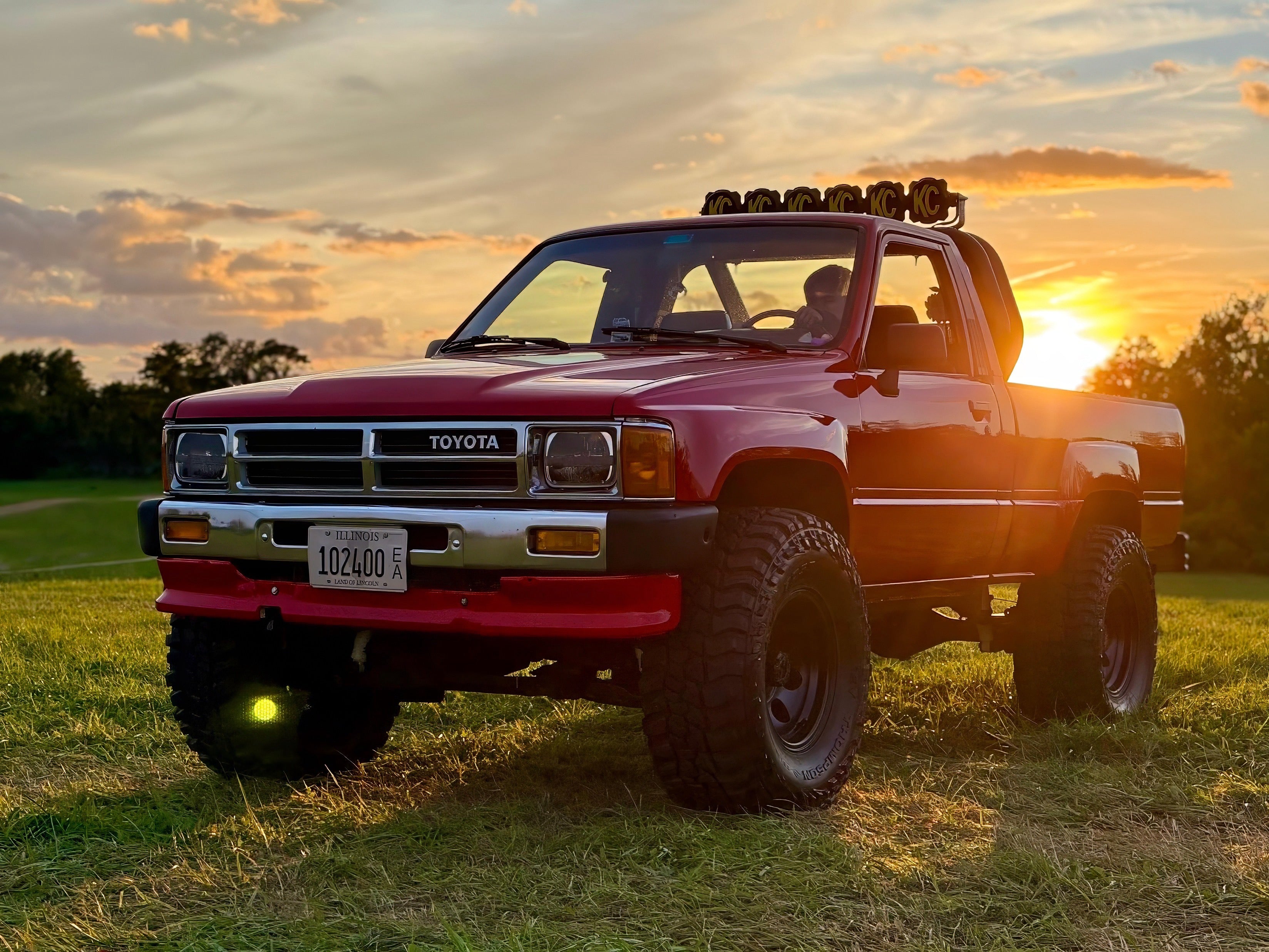 Red Custom Toyota truck on grass with sunset in the background